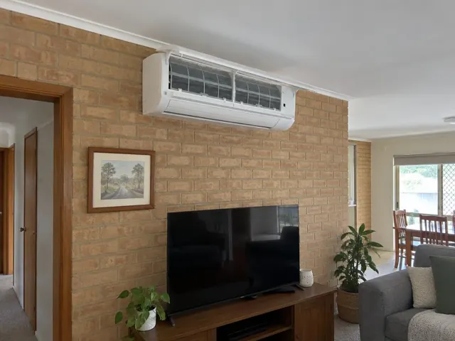 Clean split system on a brick living room wall above a TV, with filters visible behind open front panel in Munno Para