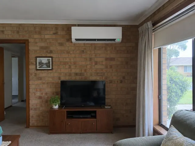 Split system mounted on a brick living room wall above a TV, with open louvre in Hillbank