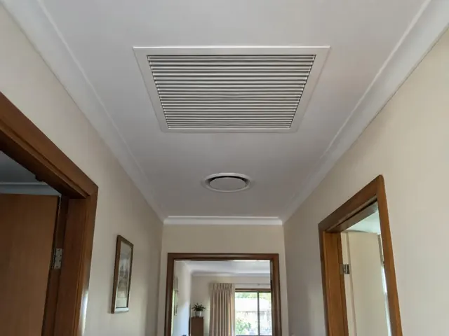 Ceiling return-air grille and round outlet in a narrow hallway with timber door frames and cream walls in Craigmore