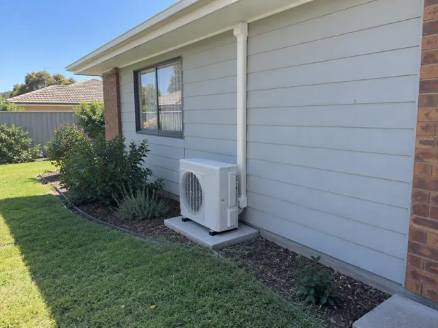 Outdoor air conditioner unit on a concrete pad beside a weatherboard house exterior in Blakeview
